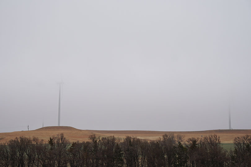 Foggy field with windmills semi visible.