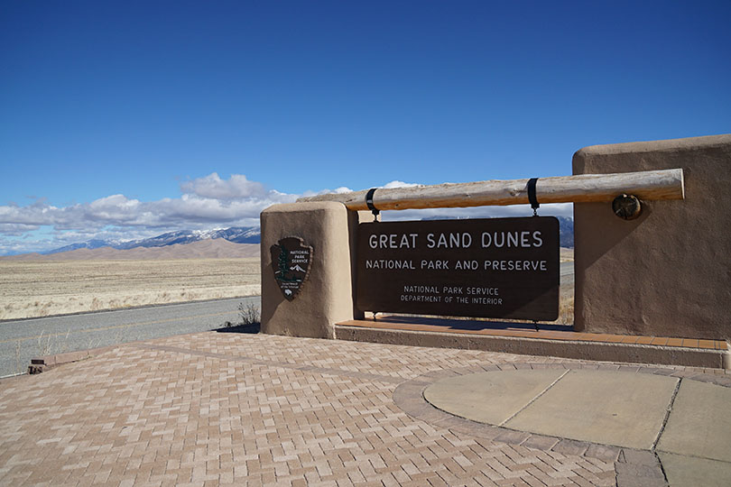 Great Sand Dunes National Park and Preserve sign with the dunes in the background to the left.